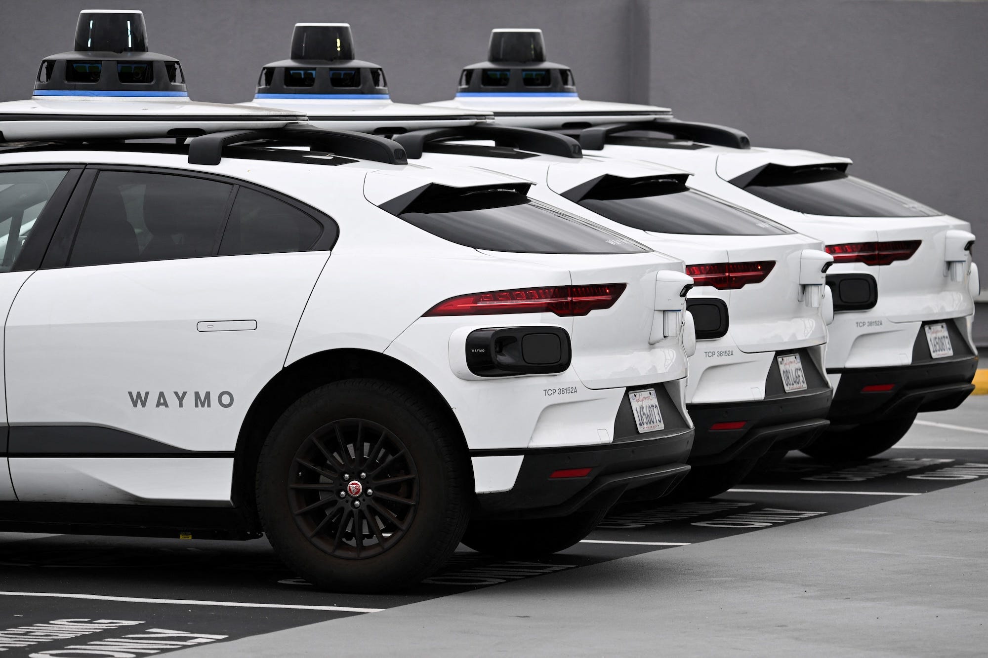 A fleet of Waymo self-driving vehicles — featuring 360-degree cameras on the roofs — sit in parking spots at an EVgo charging station.