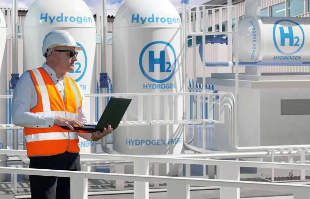 Engineer stands among hydrogen equipment with laptop to control the process of obtaining energy