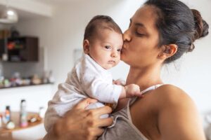 A mother holding and kissing her young baby in the kitchen.