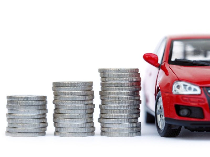 Four stacks of coins increase in height beside a premium red car isolated on white background.