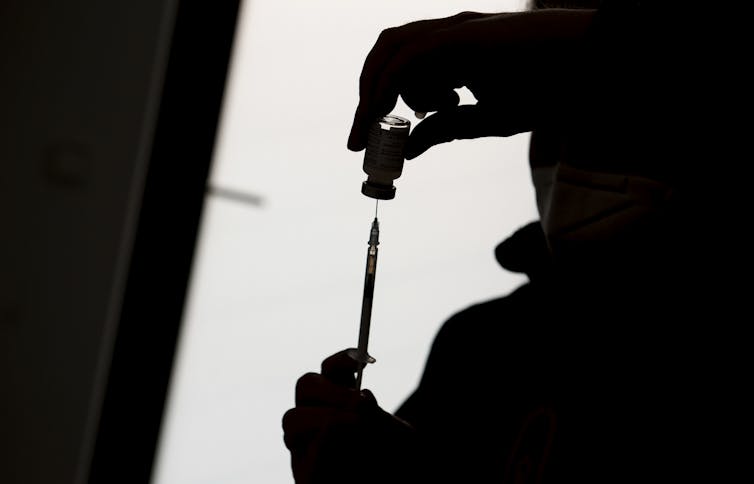 A silhouette of a person filling a syringe from a vial of vaccine