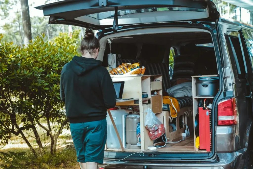 Person working on laptop in converted van with items stored in cubby holes and hanging hooks