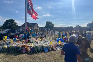 A photo of a flagpole surrounded by bouquets and stuffed animals outside of a school.