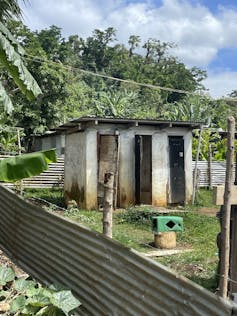 A toilet block outdoors with mountain and trees behind.