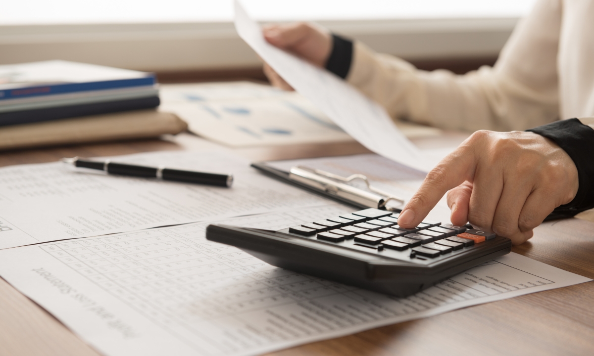 a close up of a person's hands at a desk with papers and a calculator