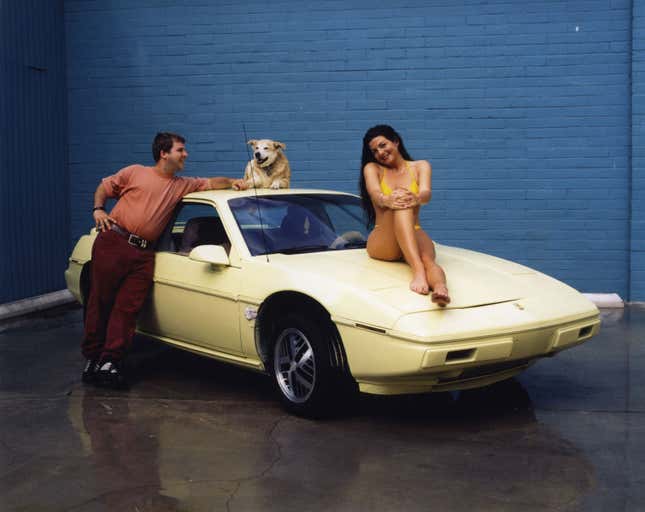 A photo of two people leaning against a yellow car. 