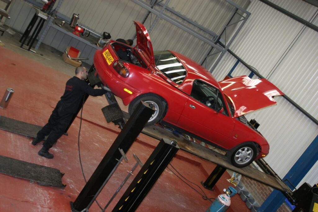 Person working on modifying a red Mazda MX-5 in a garage