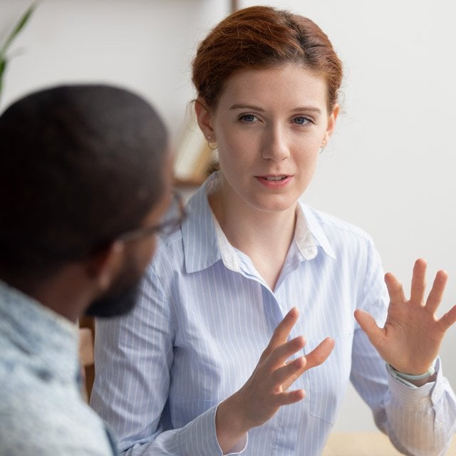 A woman talking with her hands as someone else listens.