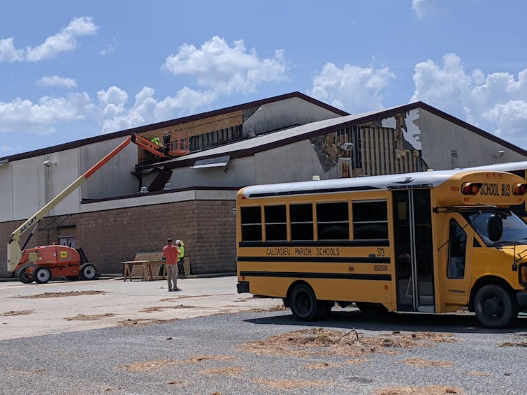 A school with sections of wall missing and a school bus parked outside.