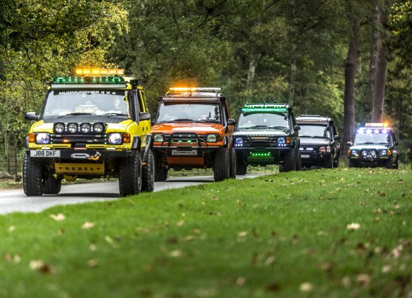 Different coloured Land Rovers in a rally driving down the road