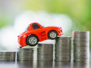 Car climbing a steep hill made out of coins to represent rising insurance costs