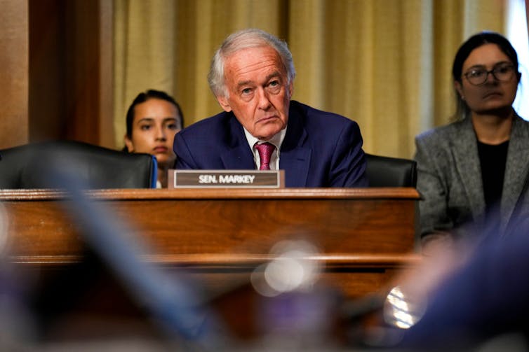 Older man wearing suit listens during a hearing.