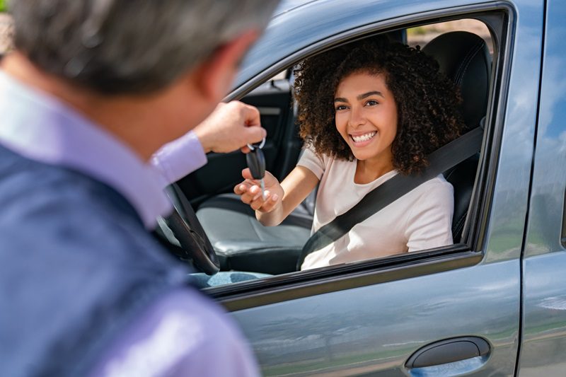 Man handing the keys of her rental car car to a happy Latin American woman