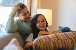 A woman listens as her daughter reads aloud from a book.