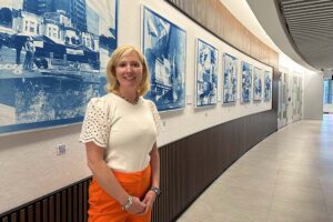 Gina Greenleaf, standing in front of some art on a curved wall