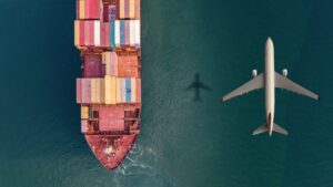 Cargo airplane flying over container ship in the ocean.