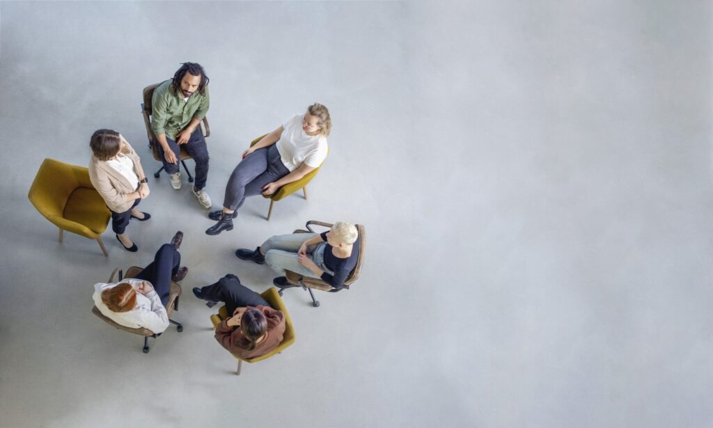 Directly above shot of a group of people sitting in circle in support group session. Young woman sharing her experiences during a mental health group therapy meeting.