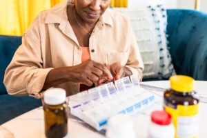 A photo of a senior woman at a table sorting her pills into an organizer.