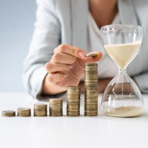 Woman in suit stacking coins on table with hourglass