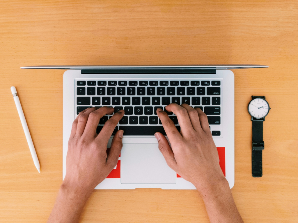 Hands typing on laptop, pen and watch placed next to it. 