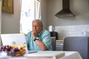 An older man, looking concerned, using a laptop computer at a kitchen table