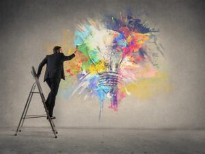 Businessman standing on a step ladder, painting a graffiti art lightbulb on a wall