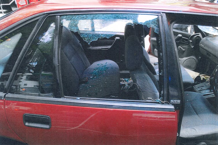 A close-up of a red car with smashed in windows.