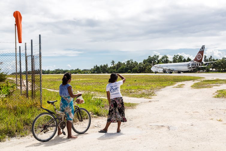 Kiribati women watch a plane arrive