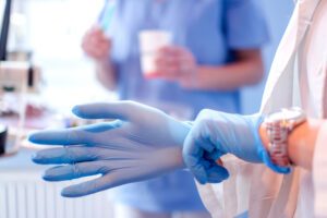 A close up photo of a doctor's hands putting on blue sterilized surgical gloves in a medical setting.