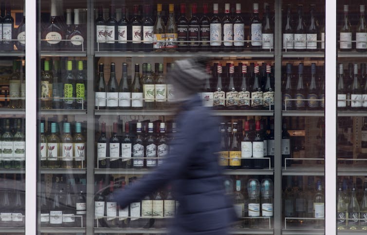 A blurred person pushing a shopping cart past a display of wine.