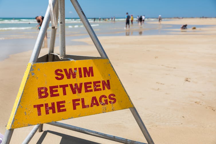 A sign on a beach says swim between the flags.