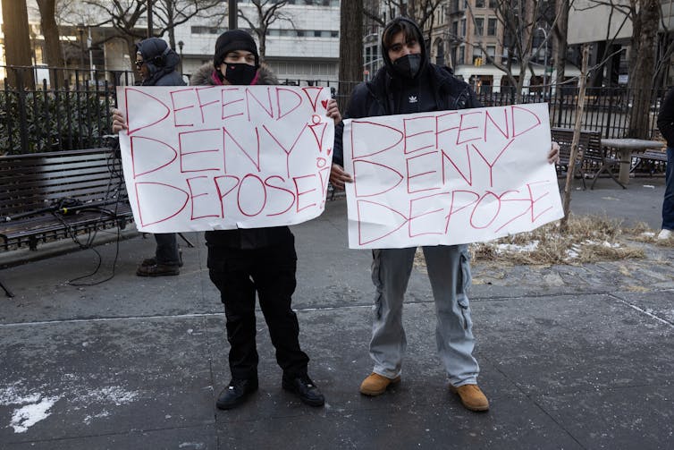 Two young men hold handmade signs that read 