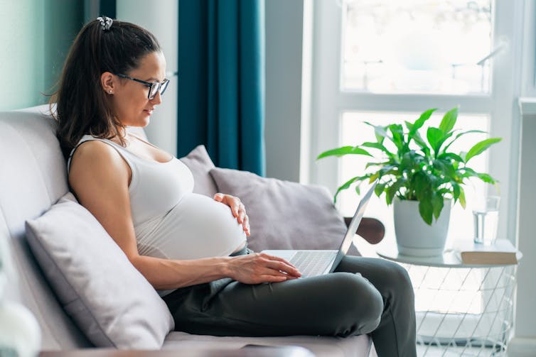 A pregnant woman sitting on a couch using a laptop.