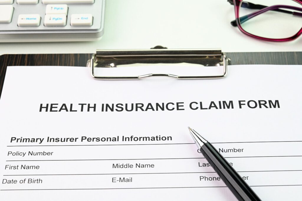 A health insurance claim form on a clipboard. A black pen rests on top.