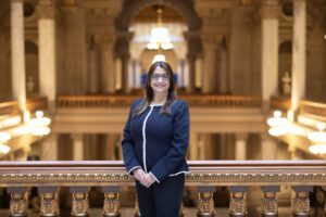 A woman wearing a blue pant suit stands by a balcony in the Indiana state house.